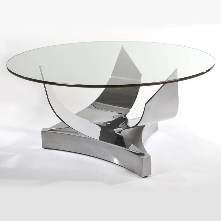 Sculptural, three-pronged, polished-stainless-steel base supports a 3/4-inch-thick round glass top. Each arm of the base comes to a small point capped with a tiny steel triangle on which the glass rests. Stunning and uncommon. Base can easily