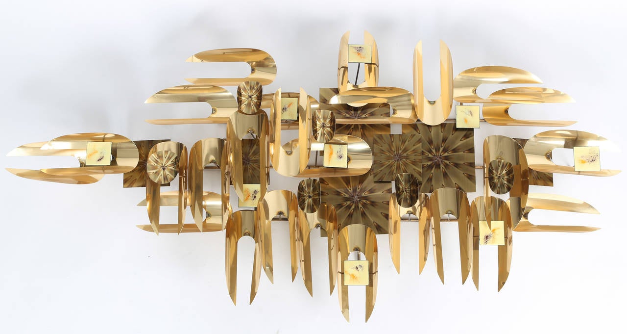 Large abstract brutalist sculpture consisting of C-shaped elements of cut and bent polished brass-plated steel, decorated brass-plated squares and circles, and enameled rectangular accents.