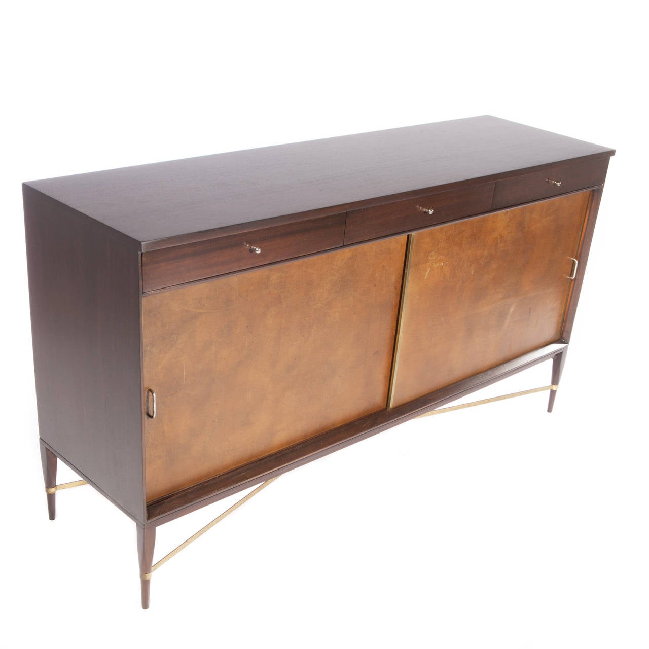 Nicely proportioned cabinet with four tapered legs with brass cross stretchers, two leather-clad sliding doors and three drawers with original brass pulls. Signed with Calvin label to inside of drawer. This item is located in our New Jersey