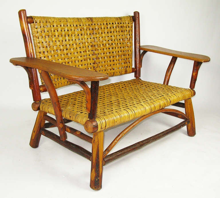 This spacious two-seat settee has a hickory pole frame with its original woven rattan cane seat and back, and generous flat oak arm or drink rests. It is in excellent, original condition.