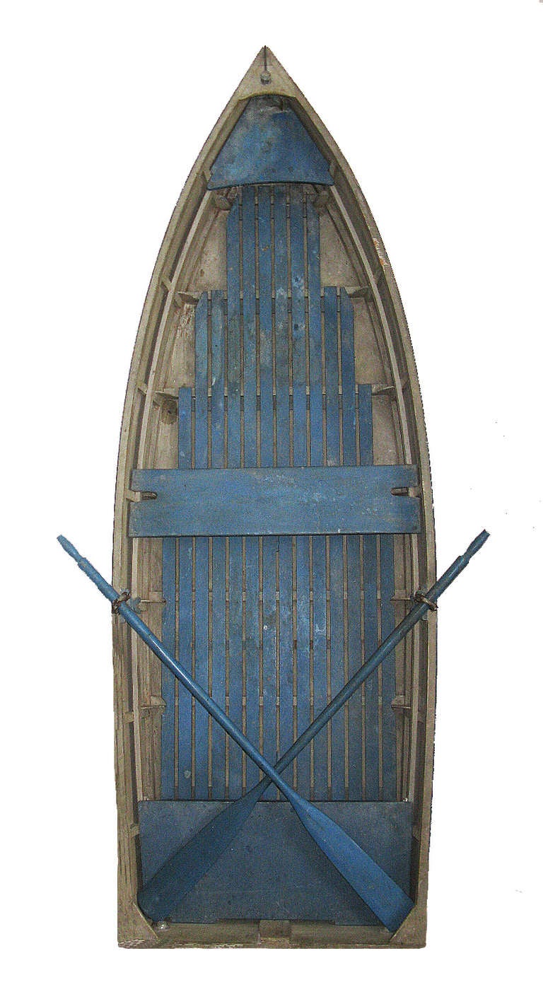 A handmade wooden boat with appealing Nantucket blue and white paint and a matching pair of blue oars. It is in great condition, and its compact 11' length makes it useful on the water or as indoor or boathouse decor. It makes a particularly