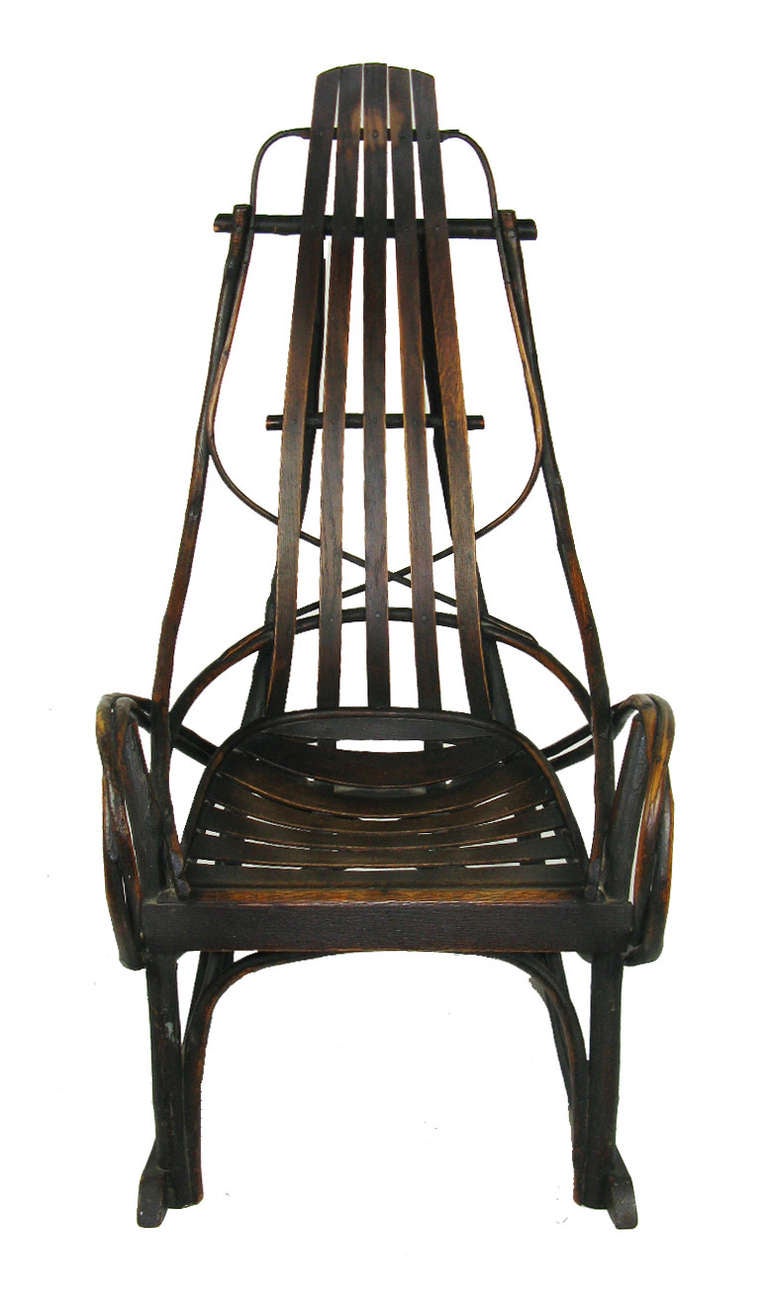 A very comfortable, old rocking chair with bent hickory twig arms and side supports, and a shaped slat seat and back. It has a warm, dark surface with just the right amount of wear.