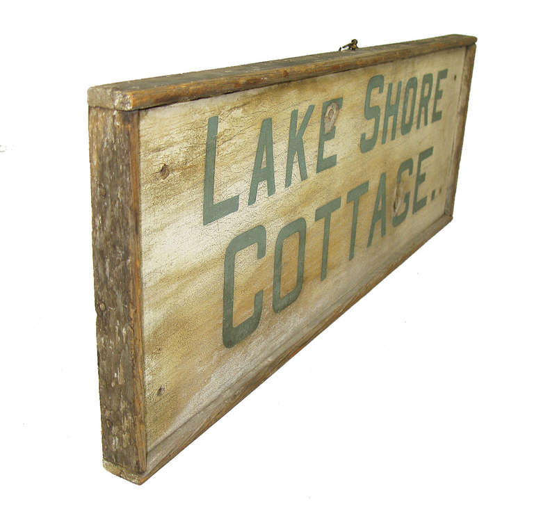 A framed wooden sign announcing Lake Shore Cottage. Both the green lettering and cream background have an appealing crackleure surface.