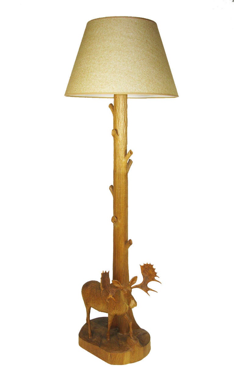 A tall rustic floor lamp with a shaft shaped by its carver to look like a tree trunk, and an accurately carved moose standing at the base. New shade. Signed by folk carver Andre Dube.