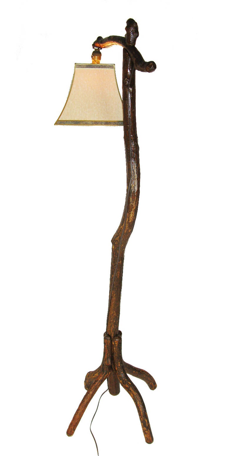 This tall bridge lamp has a natural sassafras tree branch upright and a sassafras cross-piece which holds the light fixture and shade. The legs are four applied, naturally arched sassafras branches. It has been rewired and has a new shade.