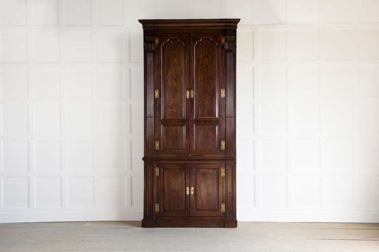 George II freestanding mahogany corner cupboard in the manner of William Kent, the upper section with two tall two panel doors with arched top, fielded panels between architectural stop-fluted columns, the doors enclosing a shelved interior, the