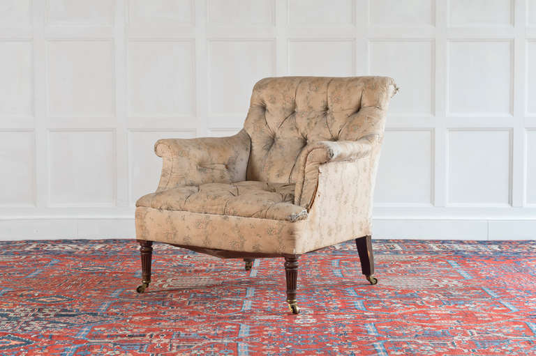A late 19th Century mahogany armchair by Bertram and Son, London, with floral upholstered buttoned back arms and seat, on turned fluted front legs with brass collars and castors. Label to the underside.