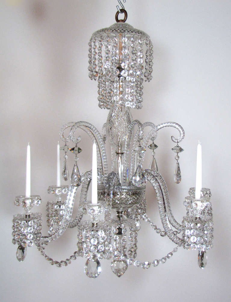 This chandelier is attributed to John Blades, glassmaker to his Majesty George III. The chandelier features multiple cascades of crystals from the top, thick cut crystal shepherd's crook arms hung with large prisms, and six cut crystal solid arms.