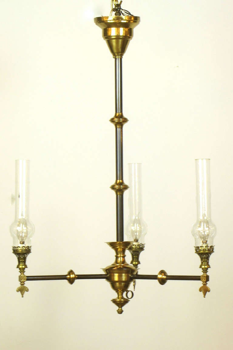 An elegant gasolier with rather sleek lines for the era.    This is made of a red brass with patinated bronze tubing. It has three lights topped with glass chimneys.