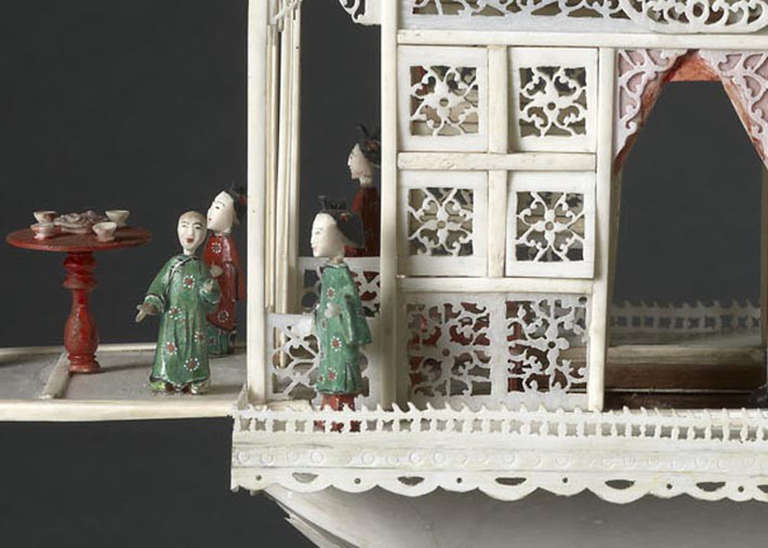CHINESE EXPORT CARVED IVORY ‘FLOWER BOAT’, the intricately pierced and carved superstructure with hinged doors and windows and with painted ivory figures, table set with cups and saucers, plants and two lanterns in the stern. On silk-covered plinth