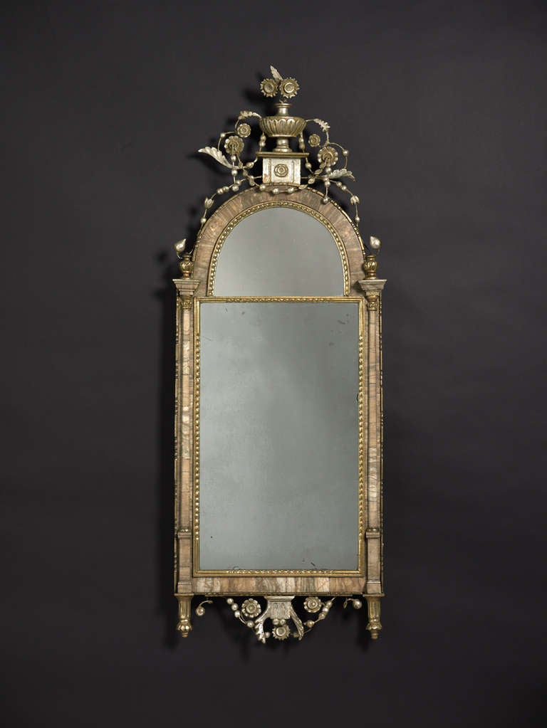 Silver-gilt and alabaster bilbao looking glass of domed, rectangular shape, surmounted by an urn on a pedestal, decorated with flowers, leaves and buds, the apron similarly decorated, further urns and pedestals on pilasters either side of the main