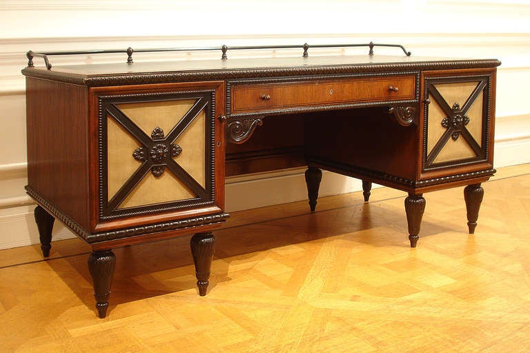 MADE BY THE VEREINIGTE WERKSTÄTTEN, MUNICH, of walnut and ebonised wood, the leathered top with deep walnut surround and broad stiff leaf edge moulding, above a central drawer with ebonised knulled border and bold scrolled brackets beneath,