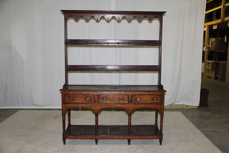 A late George III period oak high dresser with an original scalloped frieze open rack and three drawers. Turned tapering legs and raised base.