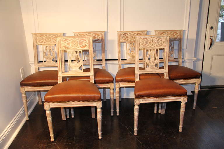 Set of six French lyre back dining chairs upholstered in cognac leather with a brass nailhead trim. Antiqued whitewash finished wooden frames.
