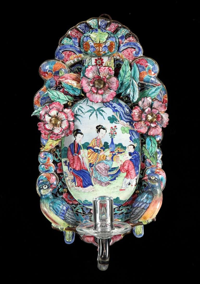 An extremely rare and magnificent pair of mid-18th century Chinese export Canton enamel wall sconces each having oval centres depicting Chinese figures in bright colors on a white background framed by three dimensional flowers, leaves and opposing