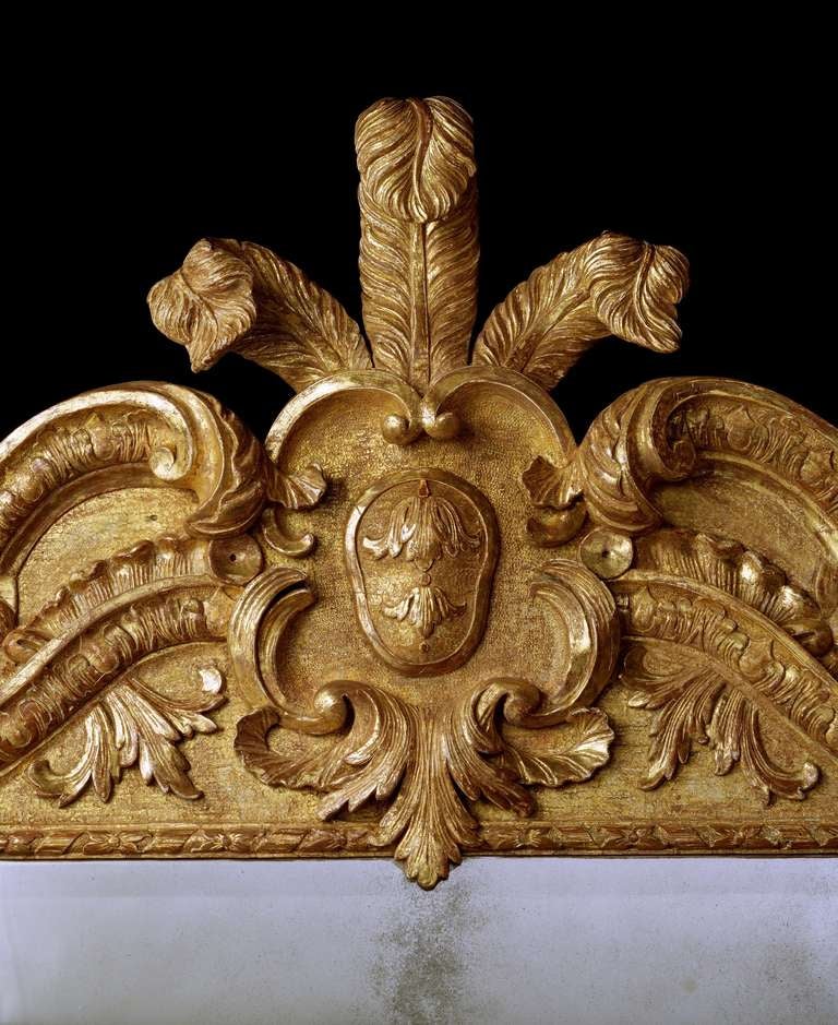 An unusual mid-18th century carved giltwood mirror in the manner of William Kent, retaining much of the original gilding and having a replaced 18th century bevelled mirror plate within a ribbon tied flower moulded edge flanked by palm fronds and
