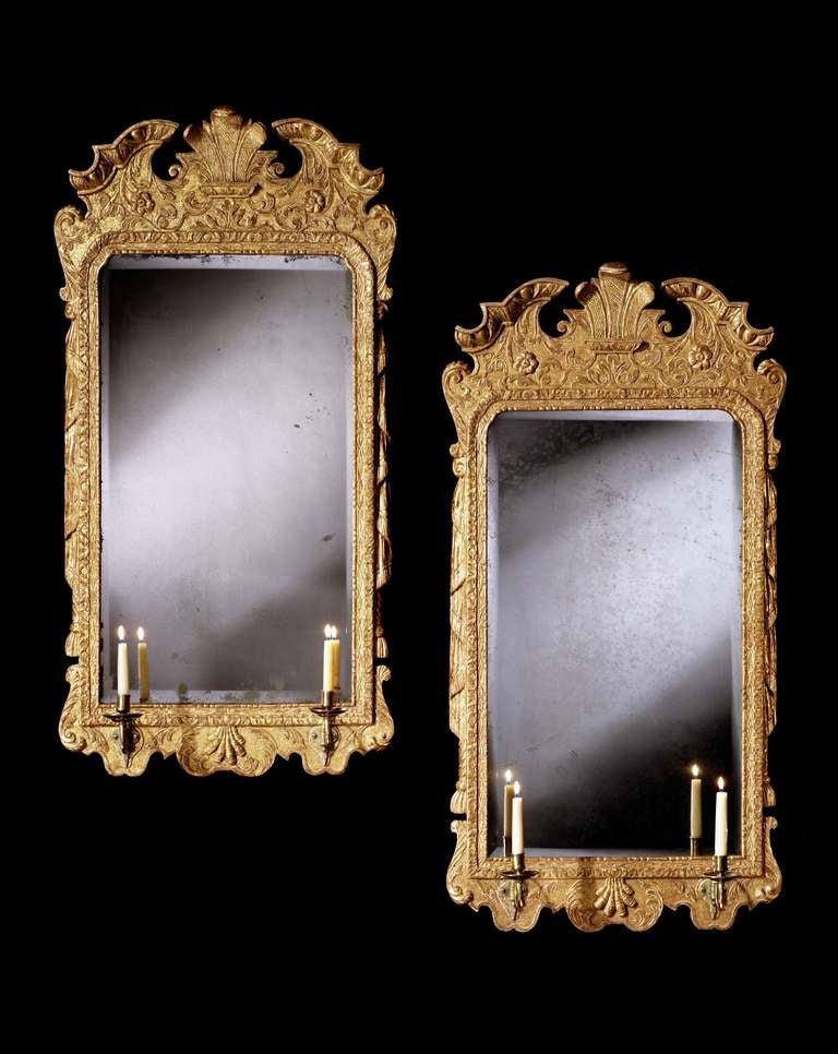 A pair of mid 18th century carved gesso girandoles, each retaining the original bevelled resilvered upright rectangular mirror plate with rounded top corners within a waterleaf moulded frame carved with strapwork and with tasselled drapes to each