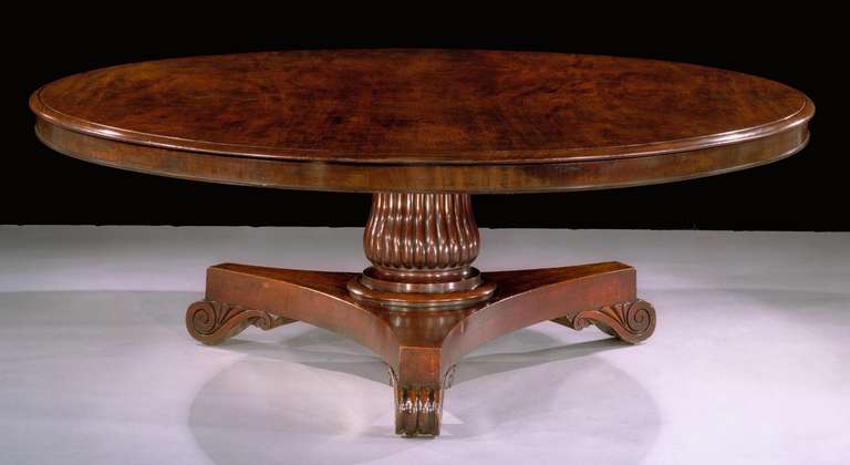 An early 19th century circular tilt-top dining table of impressive scale, on a reeded baluster stem standing on a triform base with inverted carved volute feet with concealed brass castors. 

Provenance: Norman Adams Ltd, London.

Illustrated:
