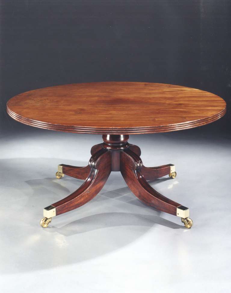 A fine quality early 19th century mahogany circular breakfast table, having a well patinated tip-up top with reeded edge; on a bulbous turned column with four moulded splay legs with lotus carved knees, terminating in the original square brass cap