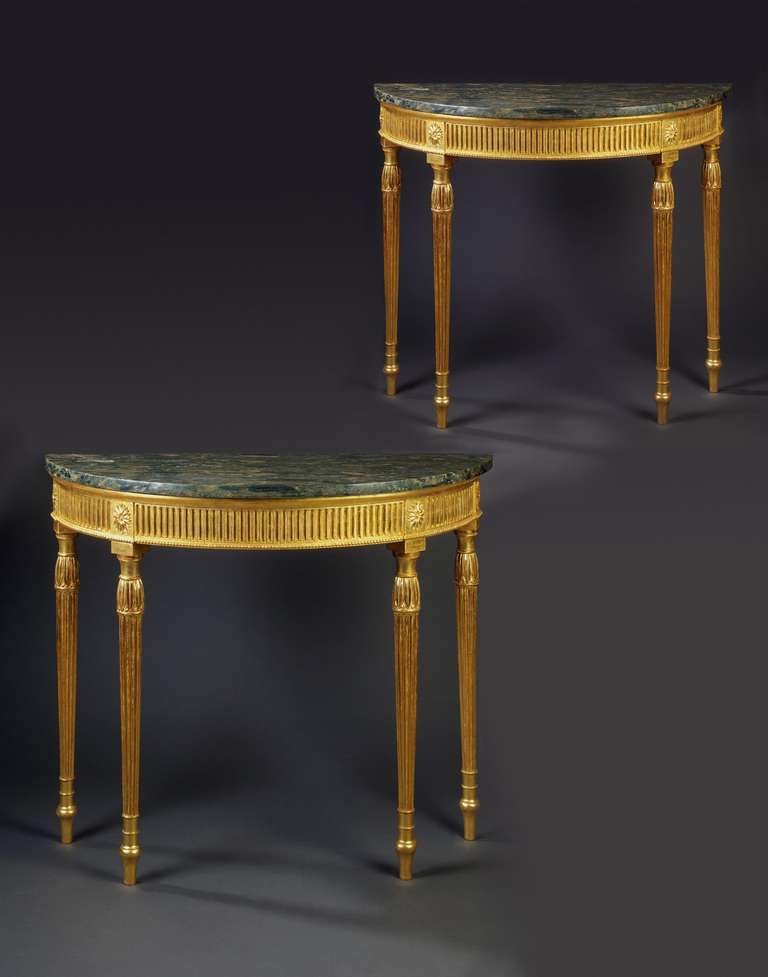 A useful pair of late 18th century Adam period carved giltwood 'D' shaped side tables, the later green Farwakir marble tops above a fluted frieze with a beaded edge, divided by plain paterae centred blocks above circular tapering reeded legs