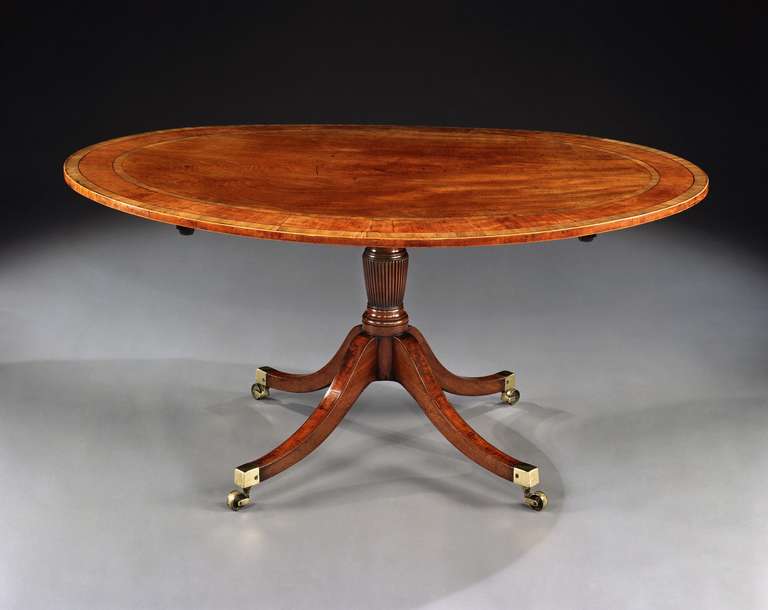 A beautifully patinated late 18th century Sheraton period mahogany breakfast table, the oval tilt-top with a broad crossband in satinwood with ebony and boxwood stringing; on a turned reeded column pedestal with four splay legs fielded with