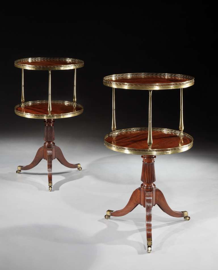 A pair of early 19th century brass mounted mahogany dumb waiters attributed to Gillows, each having two circular tiers mounted with brass pierced Greek key galleries on three bulbous column supports; on a reeded tapering column with three reeded