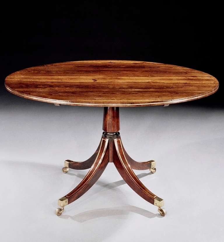 An early 19th century rosewood oval breakfast table of small proportions. The beautifully figured and faded tip-up top with cross-banded edge having gold lacquered brass moulding insert; on a turned rosewood veneered conical column with four