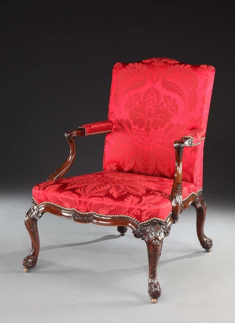 An important and well documented mid 18th century carved mahogany library armchair, having an upholstered back with shaped top and padded arms on downswept supports finely carved with floral sprays joined to the seat, upholstered in claret coloured