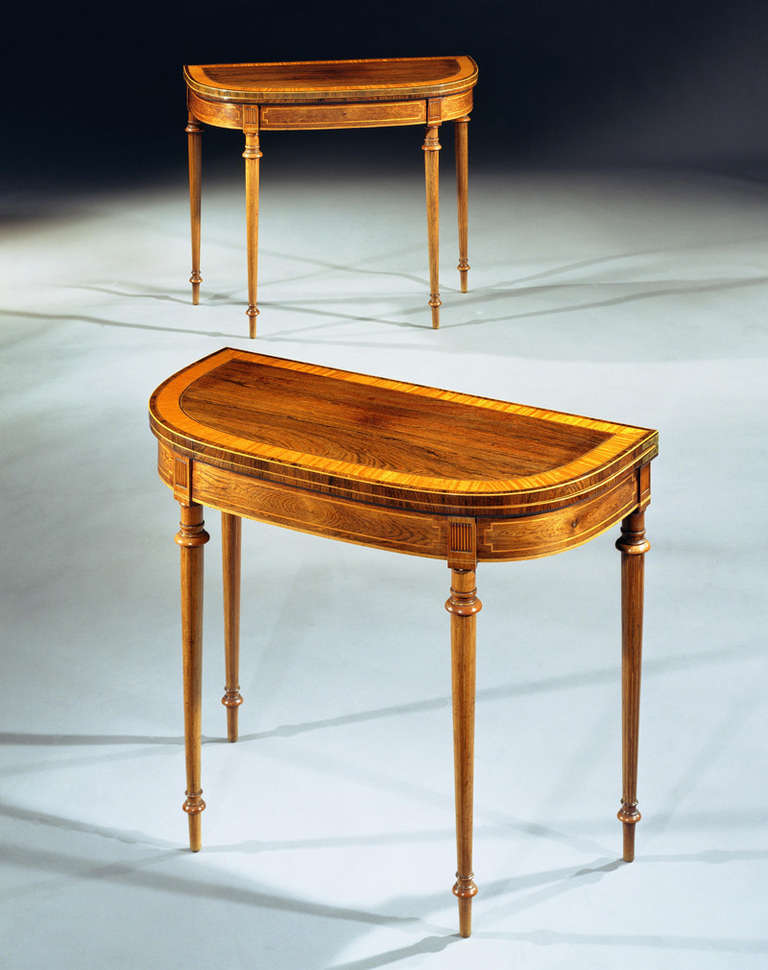 A fine pair of Sheraton period rosewood card tables with boxwood line and satinwood crossbanding, the hinged D-shaped tops above a satinwood inlaid fielded frieze, on ring-turned circular tapering inlaid legs.