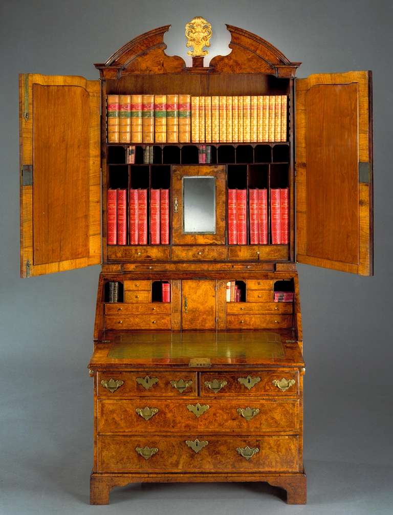 An important early 18th century walnut bureau bookcase of fine colour retaining its original brass handles, escutcheons and carrying handles, the broken-arched pediment centred by a later carved giltwood cartouche, above two doors with pilasters