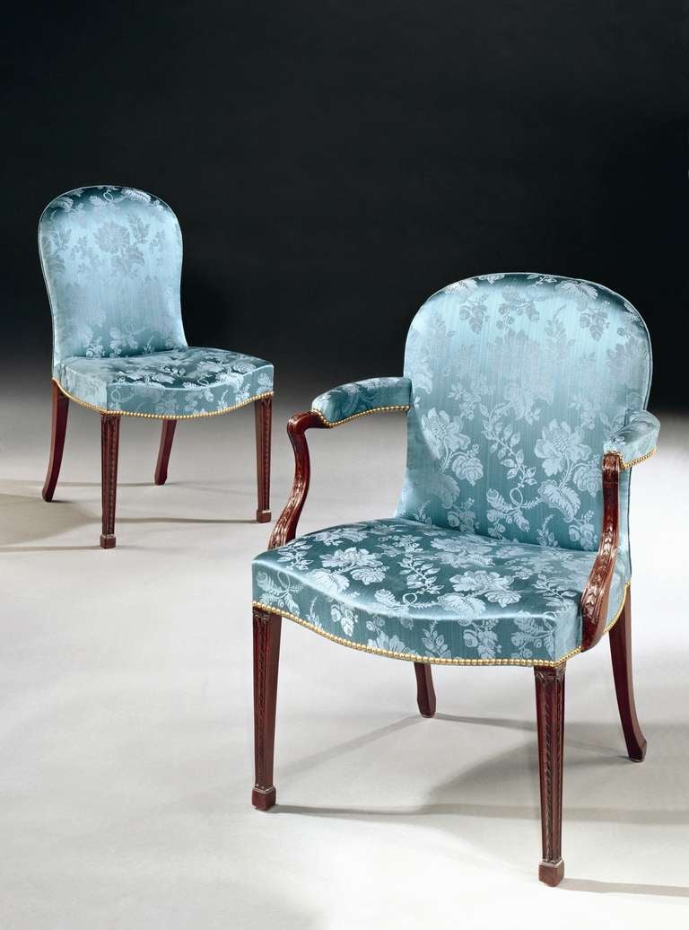 A rare set of twelve late 18th century Hepplewhite period carved mahogany dining chairs, comprising ten side chairs and two armchairs with shaped backs and saddle seats upholstered in blue silk damask; on channelled square tapering legs with husk