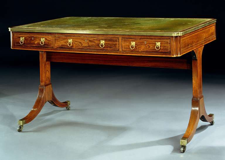 A very fine quality early 19th century ormolu mounted and boxwood inlaid rosewood writing table, the rectangular gilt tooled green leather lined top with a brass banded moulded edge above three short drawers with leopard mask ring handles and three
