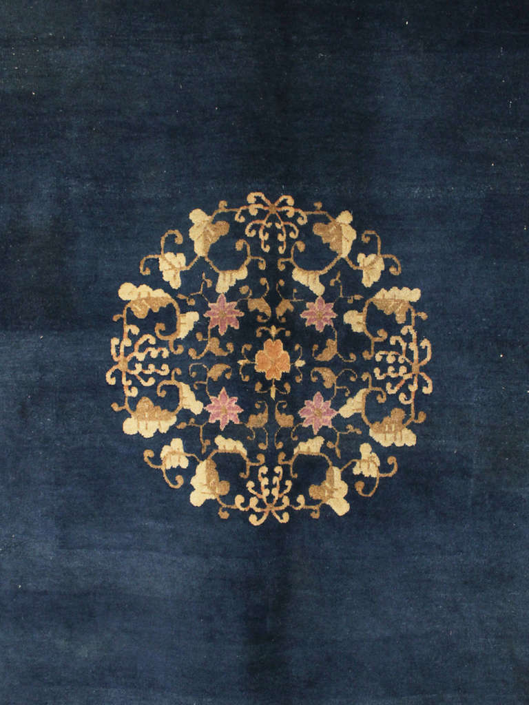 An early 20th Century art deco rug with indigo blue field presenting a central rosette composed by flowers and leaves, surrounded by a floral ivory border