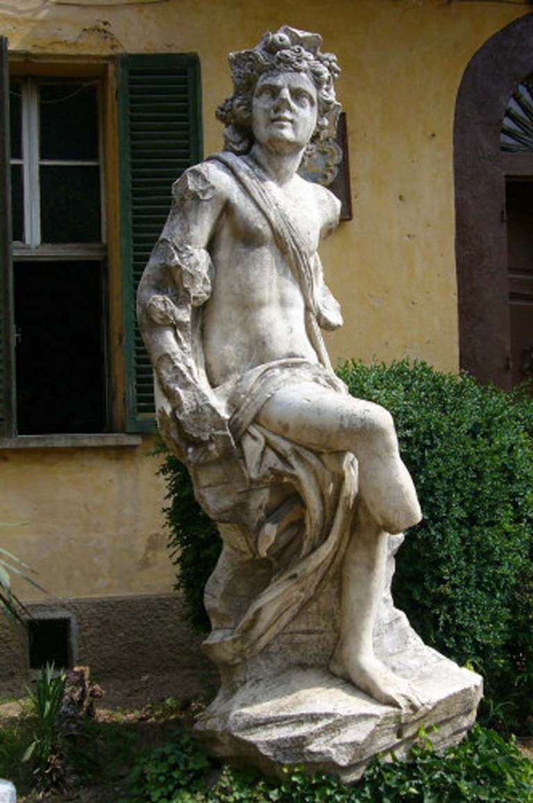 Monumental 16th Century Carrara marble statue, Bacchus is depicted at a young age as in Greek representation, allegory of autumn season, sitting on a boulder, his legs crossed, his face tilted to the right, is lifted to look up; the right arm down