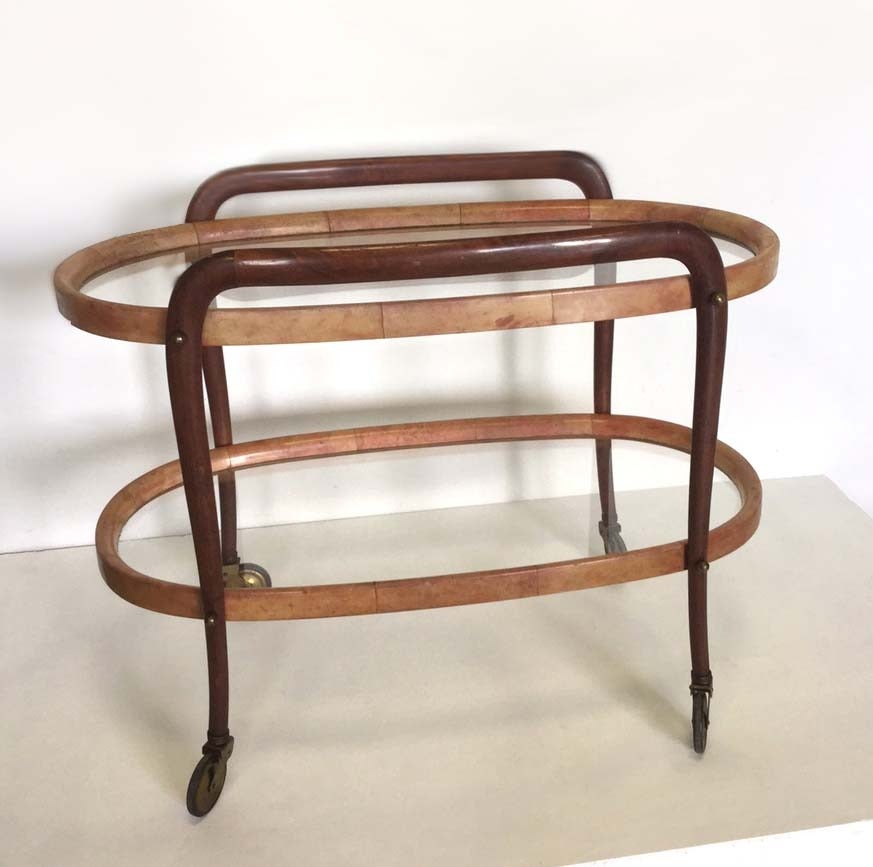 Beautiful bar cart with two oval glass shelves edge in red painted parchment ,  the legs are in mahogany curved wood with final wheels 
Designed by Aldo Tura in 1940