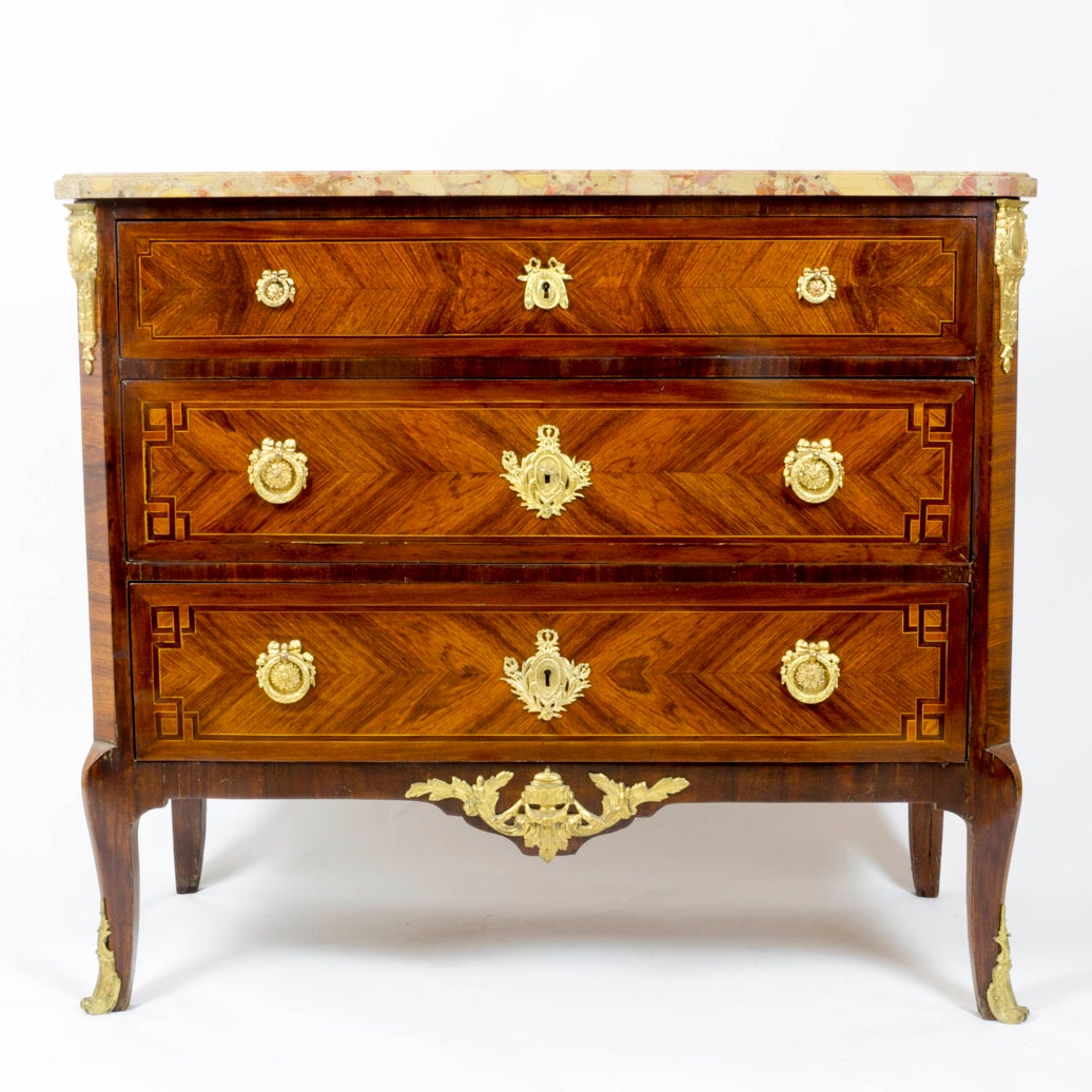 A gilt bronze-mounted kingwood and amaranth transition style commode with a moulded bre`che d'alep marble top above three long drawers, each veneered a` quatre faces and inlaid with geometric strapwork, with canted corners applied with gilt bronze