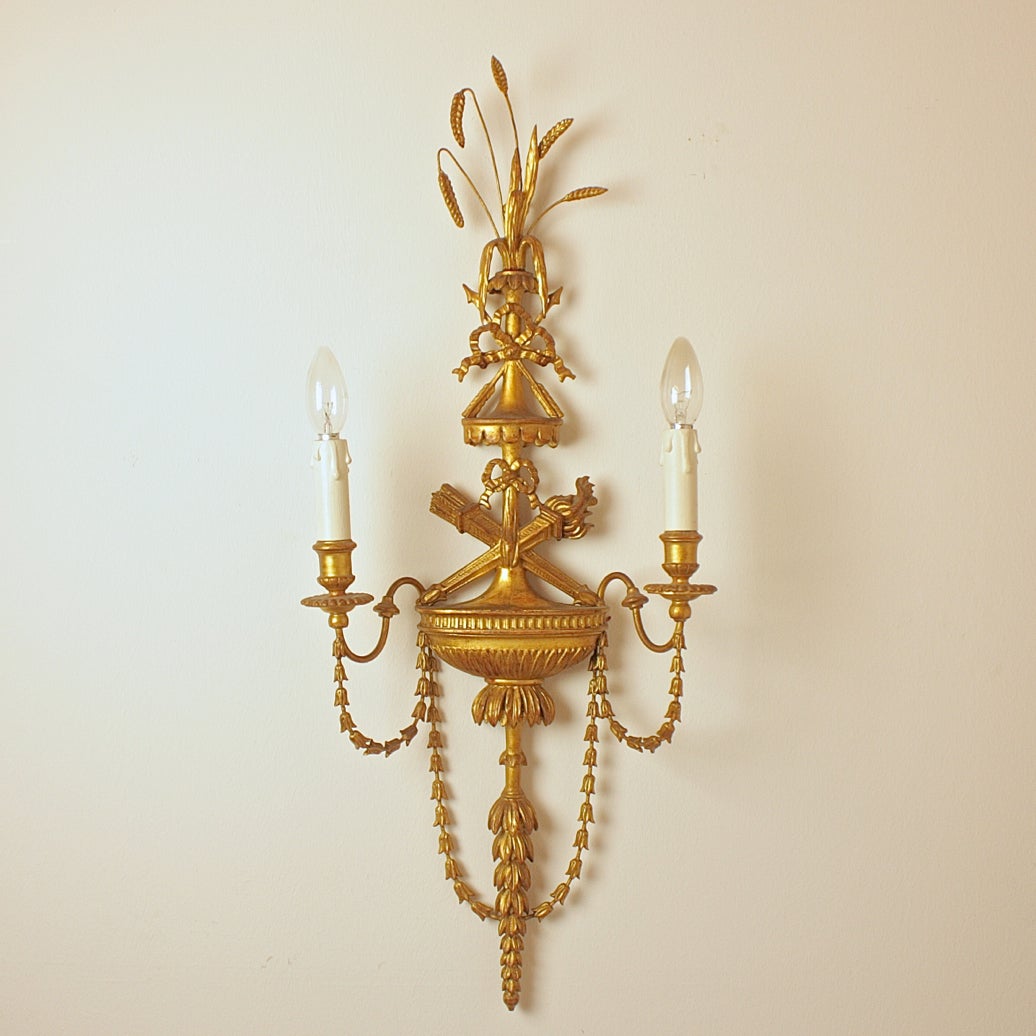 Fine water gilded Adam style wall lights, issuing two candle arms from a backplate featuring crossed torches, baldachin, ribbon and heads of crops. Excellent wood carving and in parts composition material.