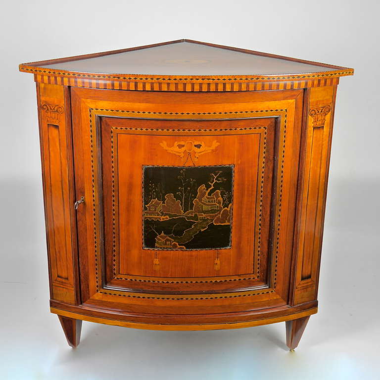 An elegant and very rare marquetry and black lacquer encoignure with a bowed front and one panel door decorated with a japanned panel of mountains and trees within a very fine marquetry of mixed exotic woods such as satinwood, tulipwood and olive