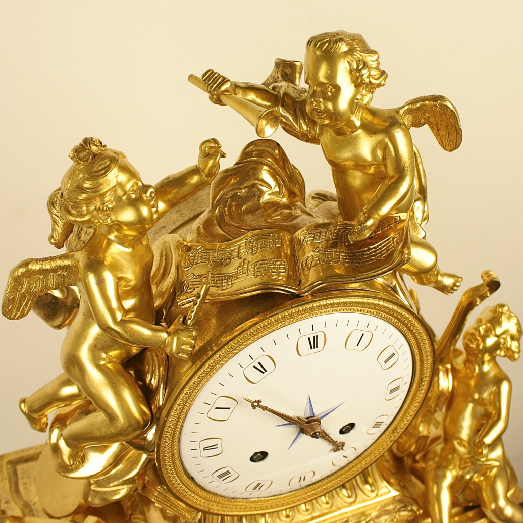 An 18th century ormolu mantel clock with a white enamel dial and Roman numerals, flanked and surmounted by three winged cherubs, each holding a musical instrument, ranging from violin to tambourine and flute, with musical notes depicting a