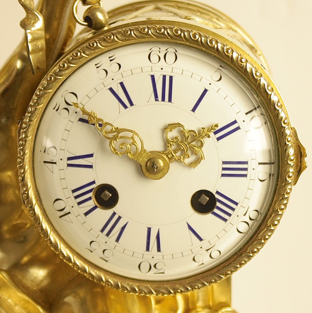 A 19th century mantle clock, the white enamel dial with Roman and Arabic numerals and elaborate pierced  hands contained within a drum case hanging from a ribbon, the drum is hold by a winged cherub sitting on a stylized cloud. Oval bronze marble