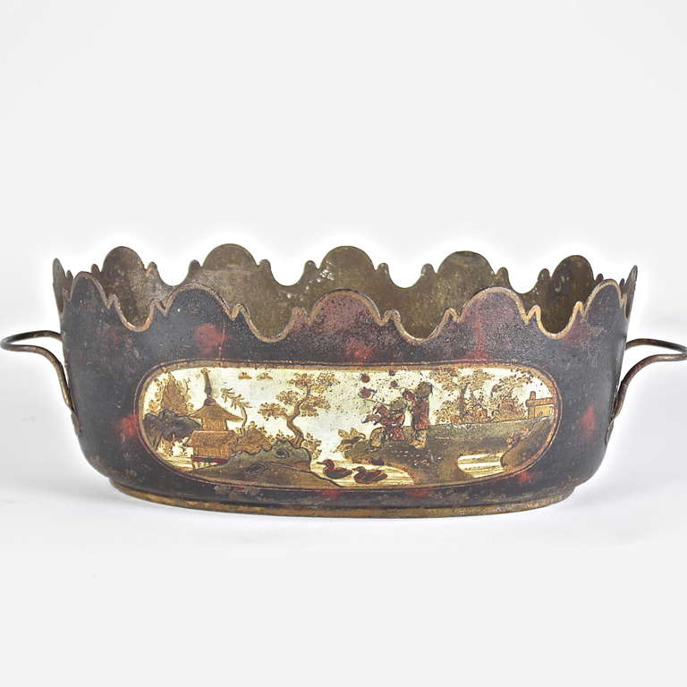 18th century French painted tole jardiniere of oval form with a crenellated edge above cartouches painted on each side with a chinoiserie scene depicting figures smoking and fishing with trees and houses, on a faux tortoise shell background, with a
