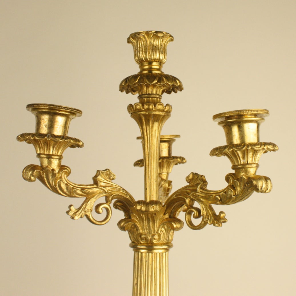 Pair of gilt-bronze candelabras each with a tapering leaf-tip cast stem supporting three foliate carved candle branches with detachable nozzles and a reeded stem raised on a tripartite base.