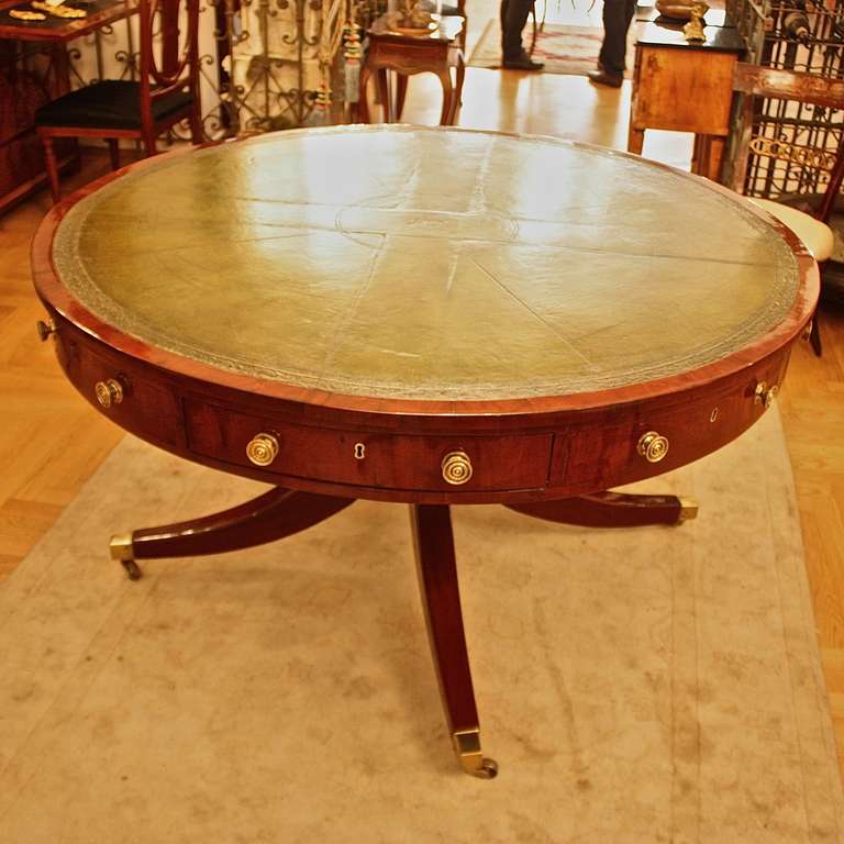 A mahogany Regency drum table, the circular original leather lined top of a lovely faded green color, fitted with four drawers between four dummy drawers, all with original handles and locks, on a ring turned column and down swept splay legs, ending