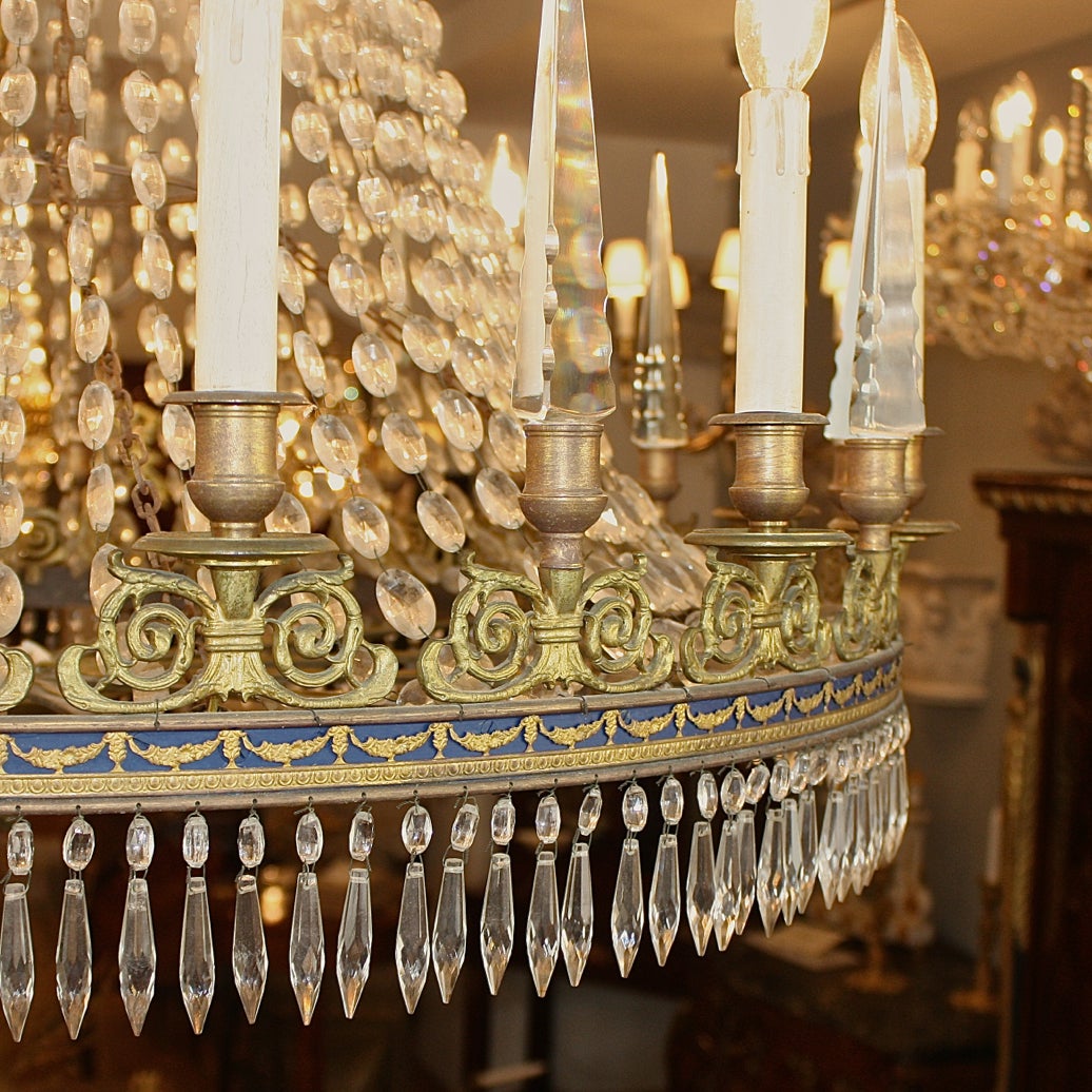 With an anthemion cast corona, hang with a chain of crystal drops with a central  ring cast with garlands and painted in Prussian blue, surmounted by acanthus cast volutes with a a candle-nozzle in its centre, alternating candles and cut-crystal