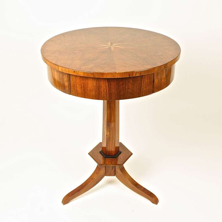 Round Biedermeier table veneered in cheerywood, top inlaid with star design, with single drawer in apron, resting on center pedestal with ebonized rim, raised on three splay legs.