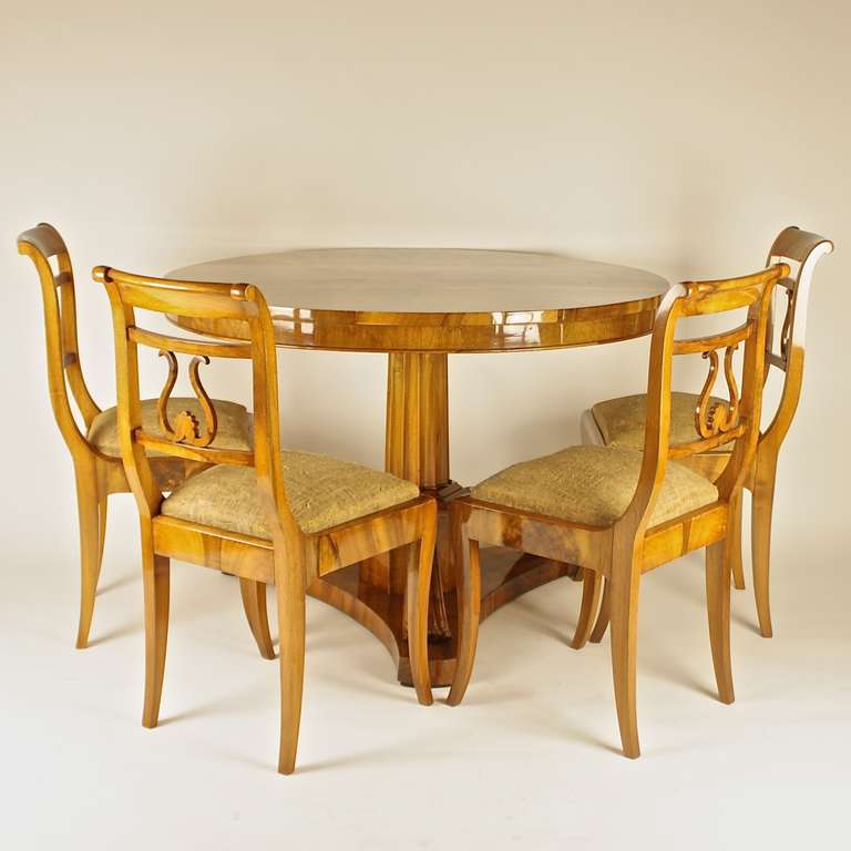 The round Biedermeier center table with a snap top veneered in walnut forming a star, on a reeded column with a hexagonal base issuing three reeded and scrolled supports reaching a tripartite plinth.
The set of four matching walnut chairs each with