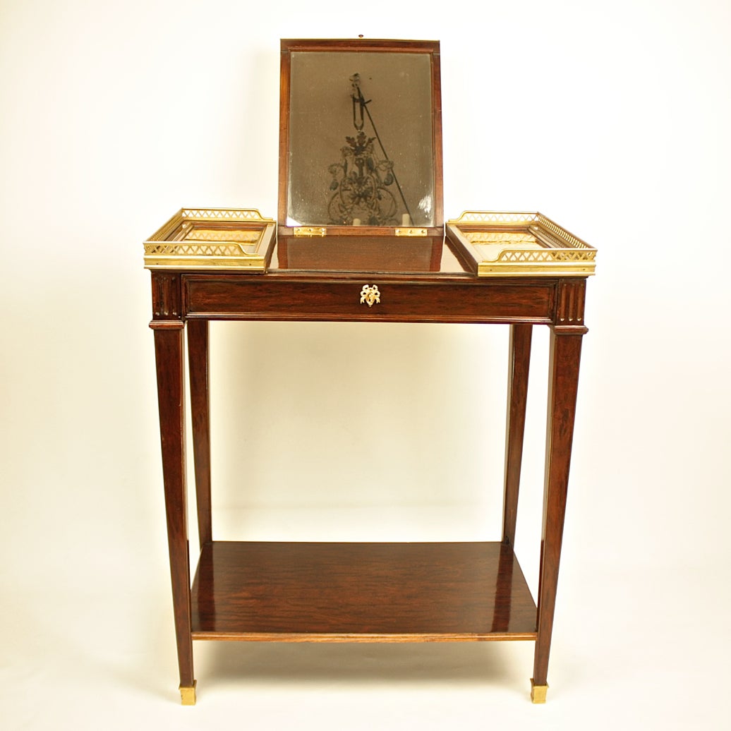 A 19th century Louis XVI style gilt-bronze mounted marquetry and mahogany poudreuse or dressing table, the rectangular top within a pierced gilt-bronze gallery, the hinged central panel enclosing a mirror, both central panel and side panel with