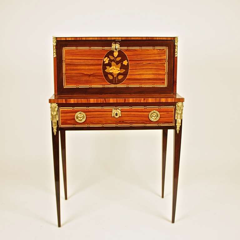 A small bonheur du jour or writing desk with a raised back section with a fall front opening, revealing an interior with the original leather lined writing surface and three small drawers, above a frieze drawer, on tall tapering legs. The desk is