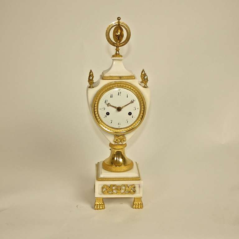 A gilt-bronze and white marble mantel clock, the white enamel dial with arabic numerals within a lyre-shaped case surmounted by four pine finials, centered by an terrestrial globe, raised on circular stem above a stepped square marble base with a