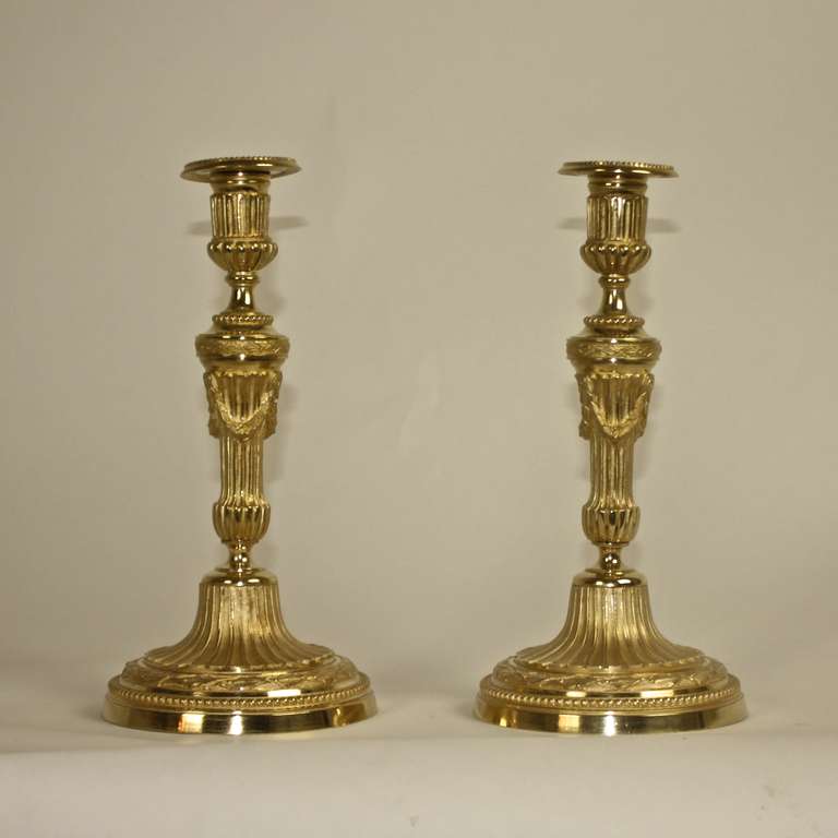 A pair of ormolu candle sticks, each with a fluted tapering stem and  fluted plinth, nozzle and base cast with foliage and pendents of fruits. Beautiful play of polished and mat surfaces. On the inside a visible inventory number.